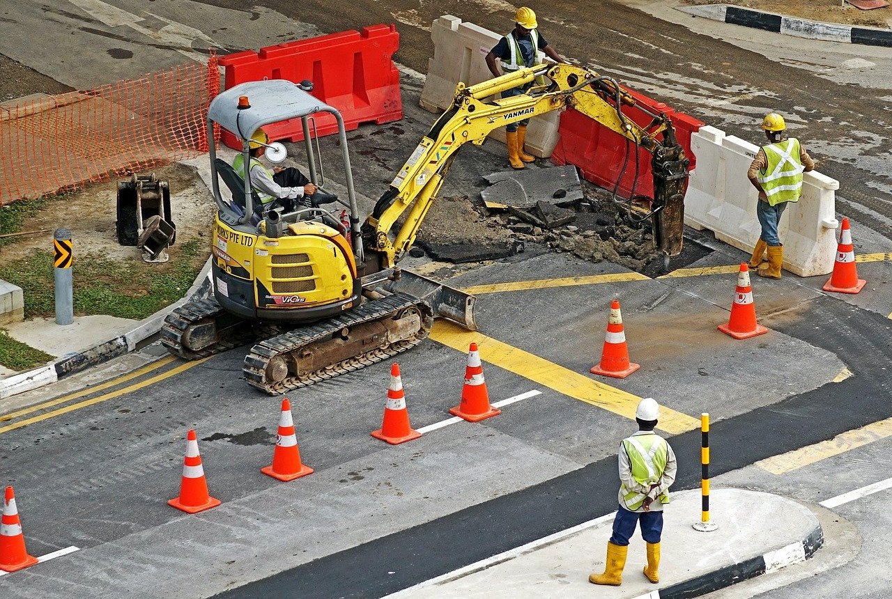 A picture of a construction crew working: one constructor worker is operating a small excavator, while three others are observing him doing his work.