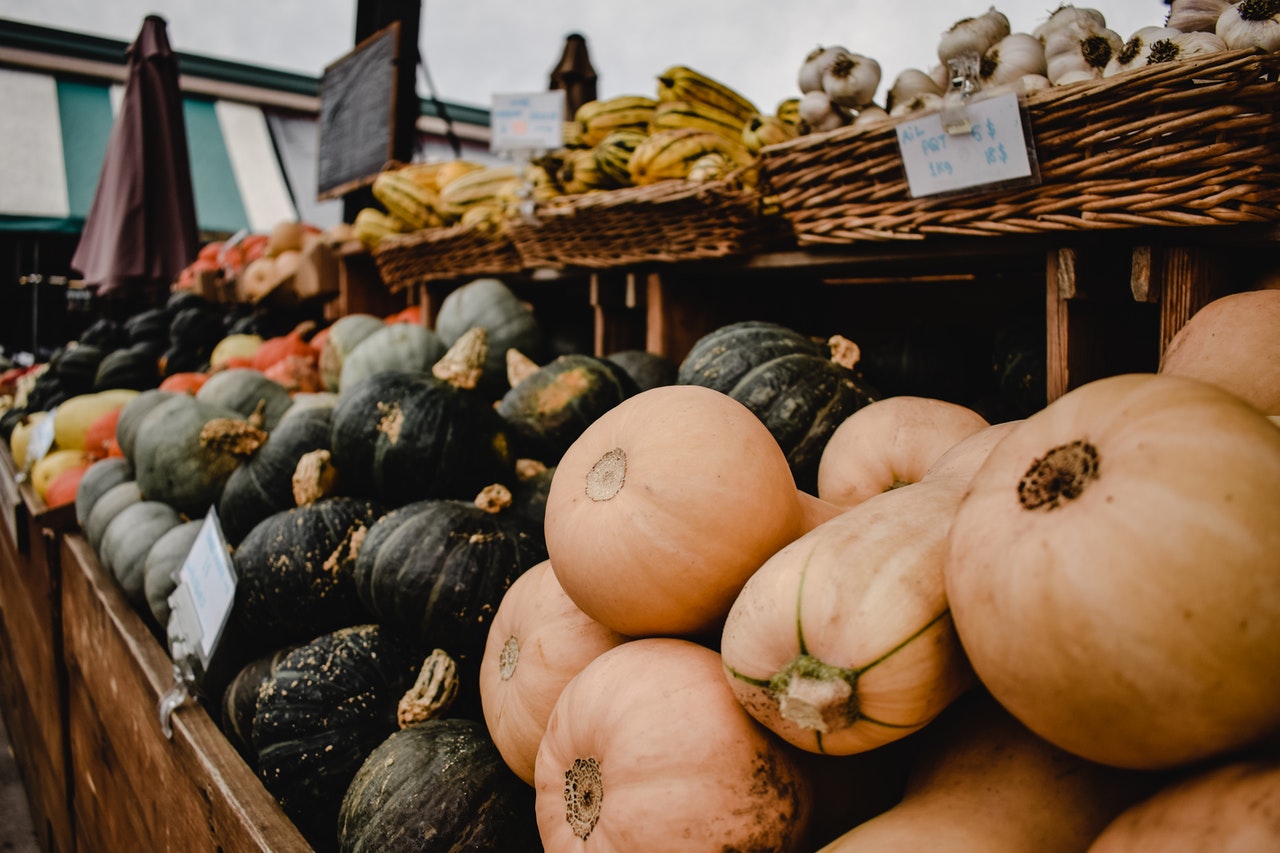 A photograph of what appears to be a farmer's market stand containing a variety of squashes, including butternut, kabocha, and delicata.