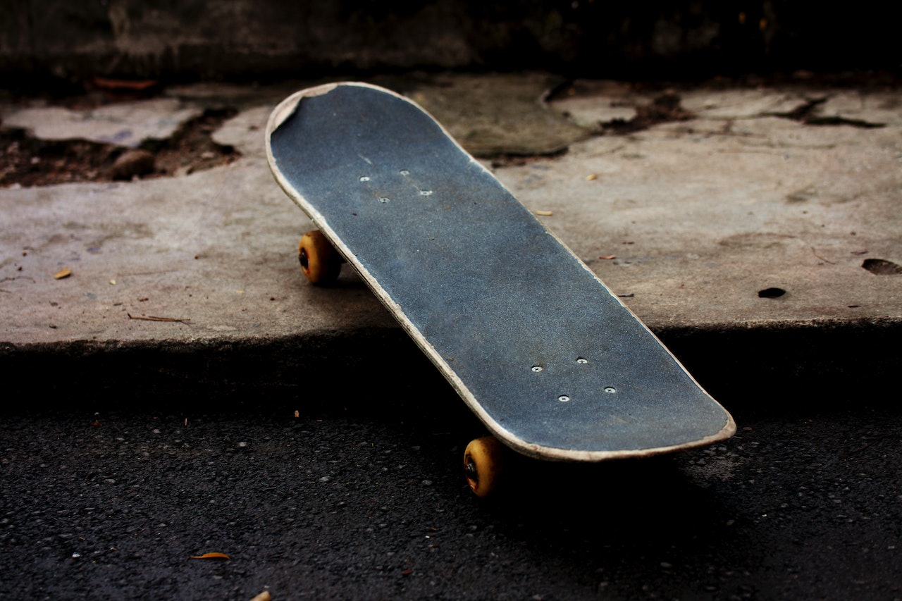A photograph of a well-worn skateboard, with its front wheels on an elevated curb and its rear wheels on the asphalt.